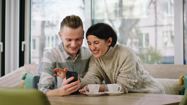 Charismatic young couple make some pictures then looking at them from the smartphone at the coffee shop