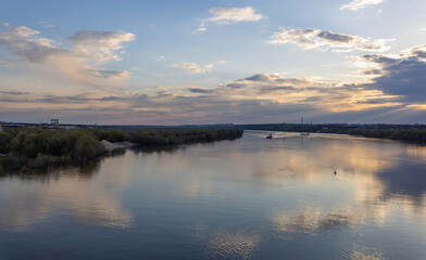 Evening landscape, sunset on the river. Wide river, horizon, clouds are reflected in the water. Sunlight through the clouds.