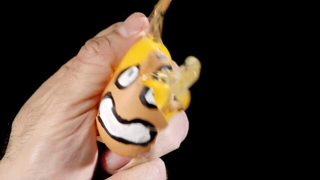 A hand crushing an egg with a drawn horrified face, killing it in slow motion. Funny horror Halloween shot, black humor, dark comedy.
