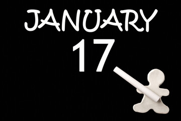 A small white plasticine man writing the date 17 January on a black board. Business concept. Education concept.