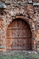 Fototapeta na wymiar Old wooden door of red color, entrance to the ancient structure, destroyed brick, fortress fragment of the gate, arch in the castle wall, historical building