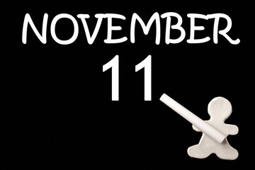 A small white plasticine man writing the date 11 November on a black board. Business concept. Education concept.