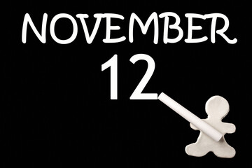 A small white plasticine man writing the date 12 November on a black board. Business concept. Education concept.