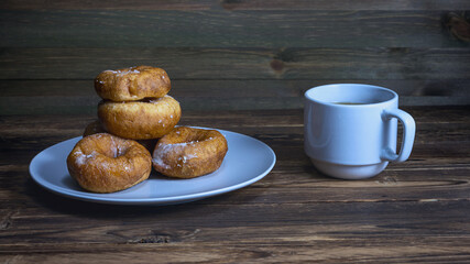 fresh delicious donuts with powdered sugar on a ceramic plate and a cup of black tea on a dark wooden surface