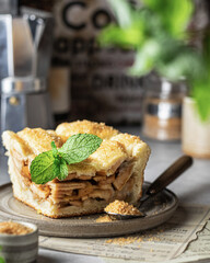 Slice of apple fruit pie on a plate decorated with mint leaf