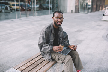Obraz premium Portrait of happy digital nomad smiling at camera during time for remote working on computer, cheerful millennial male blogger with modern laptop technology posing while doing freelance distance job