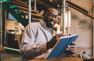 Cheerful black student in optical eyewear writing information in education notepad learning at...