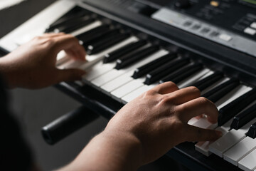 man playing synthesizer at home, taking virtual lessons, playing low notes on his piano to create a...