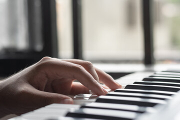 Fototapeta premium detailed view of a latin man's left hand, with his fingers on the keys of a piano playing bass notes and creating melodies on his synthesizer. practicing new sounds.