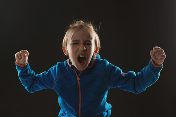 Angry boy shouting in dark. Kid mad shouting and yelling with aggressive expression and arms raised.