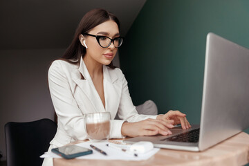 Cute beautiful business woman sit indoors in office using laptop computer.