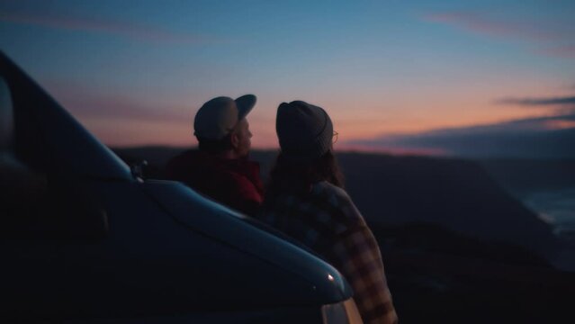 Vintage lens view, soft blurry focus on young stylish couple, travelers, friends watching colorful dreamy sunset, leaning on adventurous camper van, smelling salt ocean breeze, dreaming about future