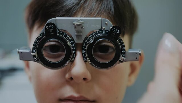 ophthalmologist examining little boy inserting a lens into lens testing eye glasses frame