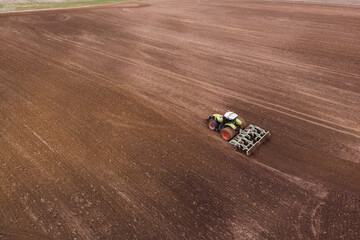 Obraz na płótnie Canvas A tractor with a disc harrow plows a field for sowing crops. Aerial photography.