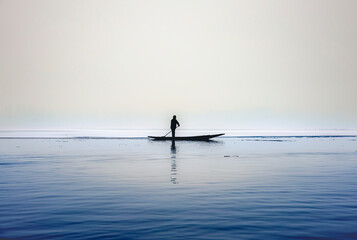 Fototapeta na wymiar Silhouette of a person in a boat(shikara) rowing in partial frozen dal lake in Kashmir, Srinagar. 
