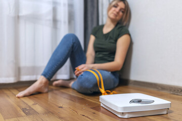 White scale and depression, upset and sad woman with measuring tape on wooden floor