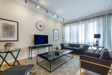 Stylish bright living room with a panoramic window. A gray armchair with a sofa, a glass coffee table and a light gray carpet.