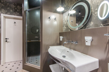 Stylish bathroom, decorated with beige and brown tiles, with a shower, sink and mirror.