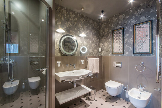 A stylish bathroom with a shower cabin, original lighting, decorated with a beige print and paintings on the wall.