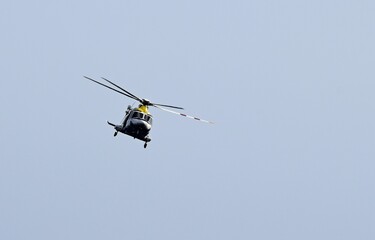 Yellow and white approaching helicopter frontal view, flying in the blue sky