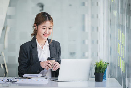 Portrait of an Asian woman holding a coffee cup Working on a tablet computer in a modern office Make an account analysis report. real estate investment information financial and tax system concepts