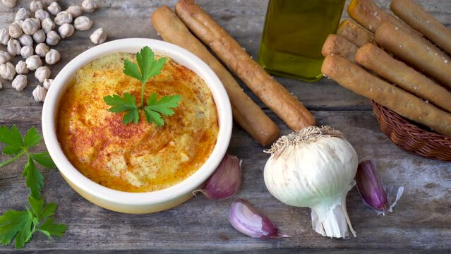 Male hand places a head of garlic next to a container with natural chickpea hummus.