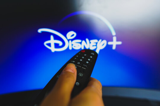 May 10, 2022, Brazil. In this photo illustration a close-up of a hand holding a TV remote control seen in front of the Disney Plus logo.