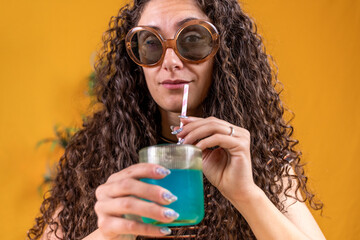 pretty woman with vintage sunglasses sitting on a table drinking blue cocktail through a straw