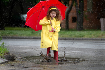 Obraz premium Little girl jumps on the pond in the rain