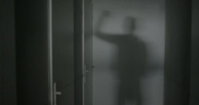 Silhouette of the shadow of a man on the wall, he knocks on the door with his hand. Dark room in the corridor of an apartment building. Signal an arrival.
