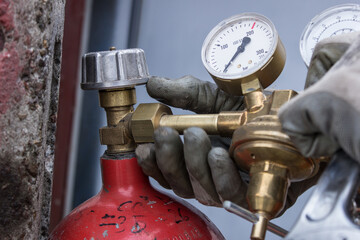 Red bottle for storing liquefied gas. Gas cylinder. Close-up plan of Men's hands in gloves screwing the reducer on the gas cylinder. Concept for content about fuel, gas or welding.
