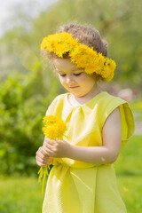 portrait of cute little girl with wreath and bouquet of yellow dandelions in park. happy child with...