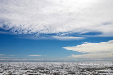 Lake Ladoga covered with ice in front of the icebreaker. The sky with light cirrus clouds is reflected in the water