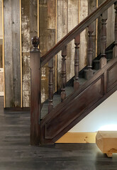 Ancienne rampe d'escalier en bois brun. Mur avec des planche de bois de grange pour donner un cachet vieillot. Balustrade dans un bâtiment de style saloon, far west.