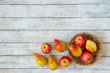 Ripe fruits apples and pears in the basket on a white wooden table. Copy space, top view.