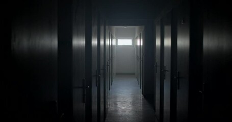 Camera movement narrow dark corridor mental hospital. Glare on doors and on floor. Light from window at the end tunnel. Many chamber doors locked. Location of dangerous people.