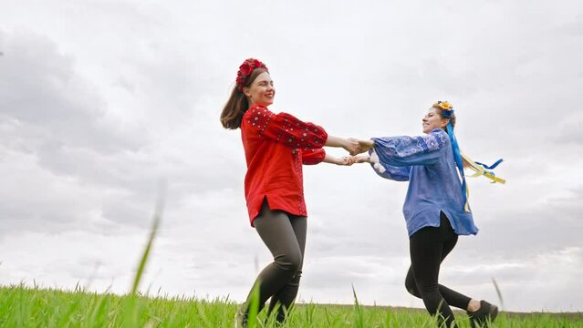 Happy ukrainian women rotating, dancing, playing and holding hands in green field. Young friends in embroidery vyshyvanka - national blouse. Ukraine, friendship, happiness, luck and fun