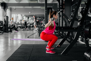 The girl does squats with a barbell in the gym.