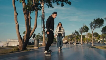 Hipster couple skateboarding. Young couple skateboarding in the street. Couple having fun with skateboard on beach. - Powered by Adobe