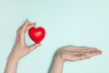 Health, medicine and charity concept - close up of female hands with small red heart and palm for your offers.