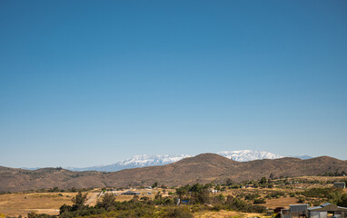 Temecula, CA, USA - April 23, 2022: Snow covered San Jacinto mountains viewed from rural area north of Temecula under blue sky, with brown hills and horse ranch up front.