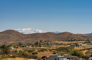 Temecula, CA, USA - April 23, 2022: Snow covered eastern part of San Jacinto mountains viewed from rural area north of Temecula under blue sky, with brown hills and ranches up front. - Powered by Adobe