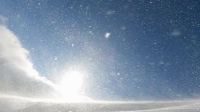 Closeup of snow storm, snow blizzard and snow drift on the mountain slipe during cold winter morning with the sun rays shining through. Slow motion