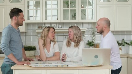 Two twin sisters are discussing in kitchen with husband purchase or renovation of an apartment. Relatives look at drawing on table and design project on laptop. Happy people at home every day