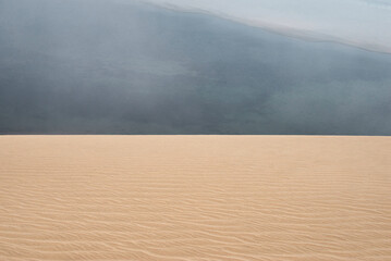 Abstract picture of dunes in the foreground and a dark blue lagoon in the background creating a perfectly divided picture with yellow and blue colors. Abstract wallpaper for presentations or desktops.