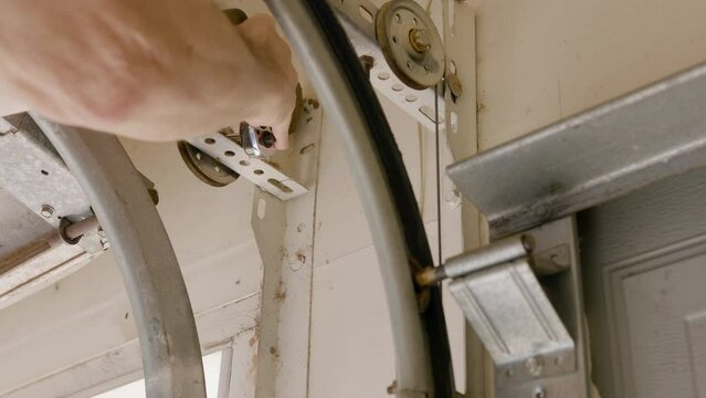 A homeowner handyman type removing an old pulley from the garage door opening system in order to install a new one.