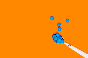blue chocolates inside a white spoon on an orange background. wallpaper to use text. graphic resource.