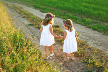 Two little sisters are walking along a country road holding hands. Girls in white dresses with...