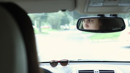 female driver eyes in mirror. young woman driving car on crossroad, looking side to side, turning vehicle. brunette student face in car mirror. caucasian girl driver. brown sunglasses on dashboard