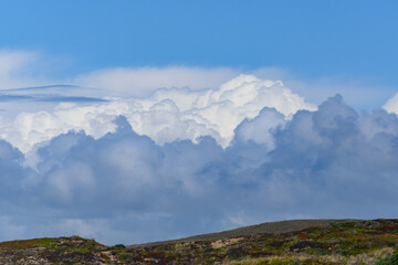 Fototapeta premium Bright blue cloudscape with huge clouds above a green gold hillside suitable for background or wallpaper